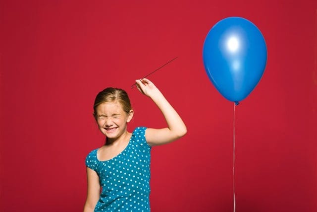 young girl with eyes closed ready to pop a blue balloon